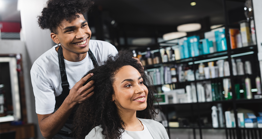 A young male hairdresser smiling as he styles the hair of a woman