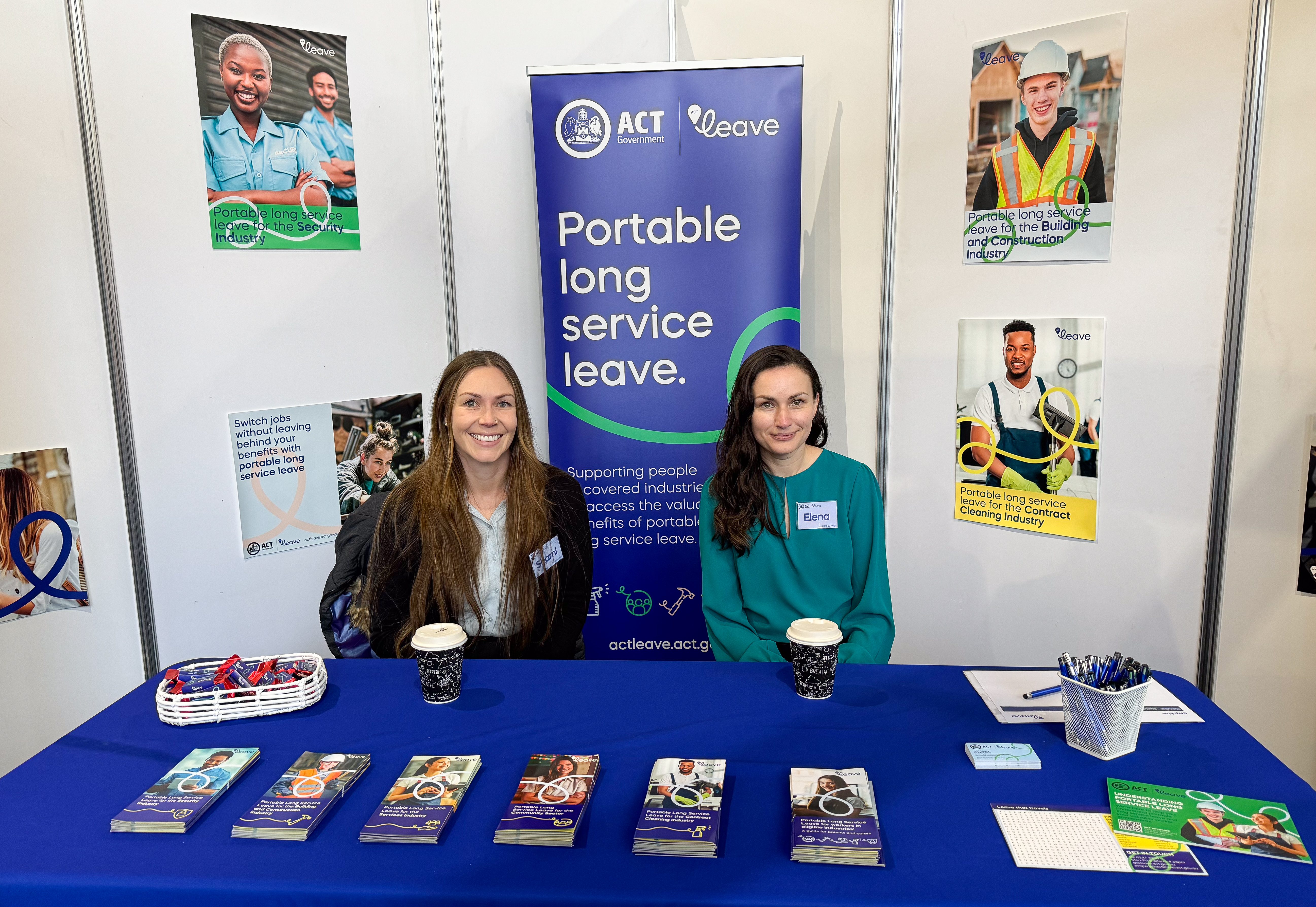 ACT Leave staff at the Canberra Careers Expo in 2024. Staff are smiling and sitting behind a table with ACT Leave brochures and merchandise displayed on top. The tablecloth is bright blue with ACT Leave logo on it